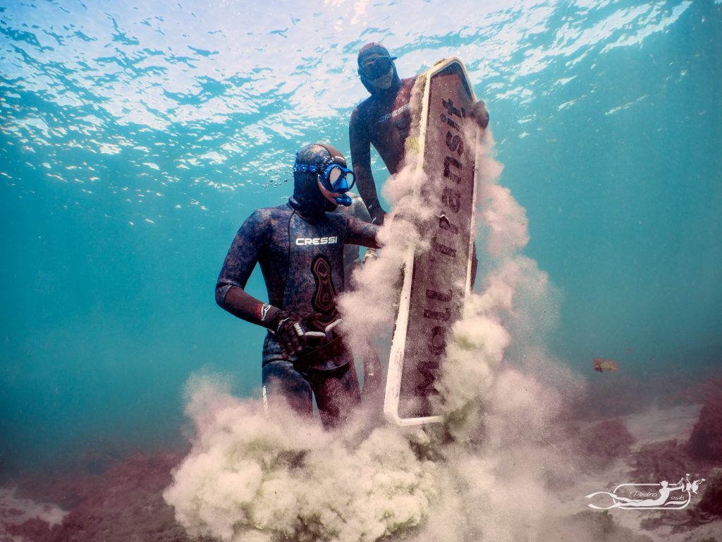 Dos buceadores haciendo submarinismo, cogiendo una señal de tránsito del fondo marino