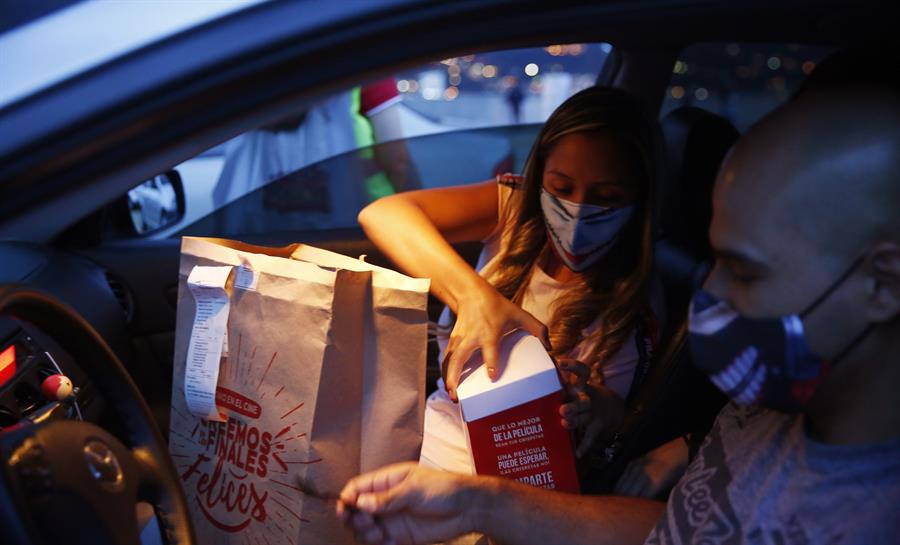 Imagen de una pareja sentada en la parte delantera de un auto, apunto de cenar comida que han traido de algun sitio de comida ràpida.