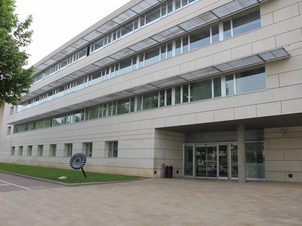 Façana principal d’un edifici modern de quatre plantes amb revestiment clar i finestres horitzontals. Davant l’entrada hi ha una vorera ampla i una escultura metàl·lica amb forma de turbina. Es veuen arbres a l’esquerra i gespa al voltant de l’edifici. L'edifici és l'Escola Politècnica Superior de la Universitat de Lleida, al Campus de Cappont.