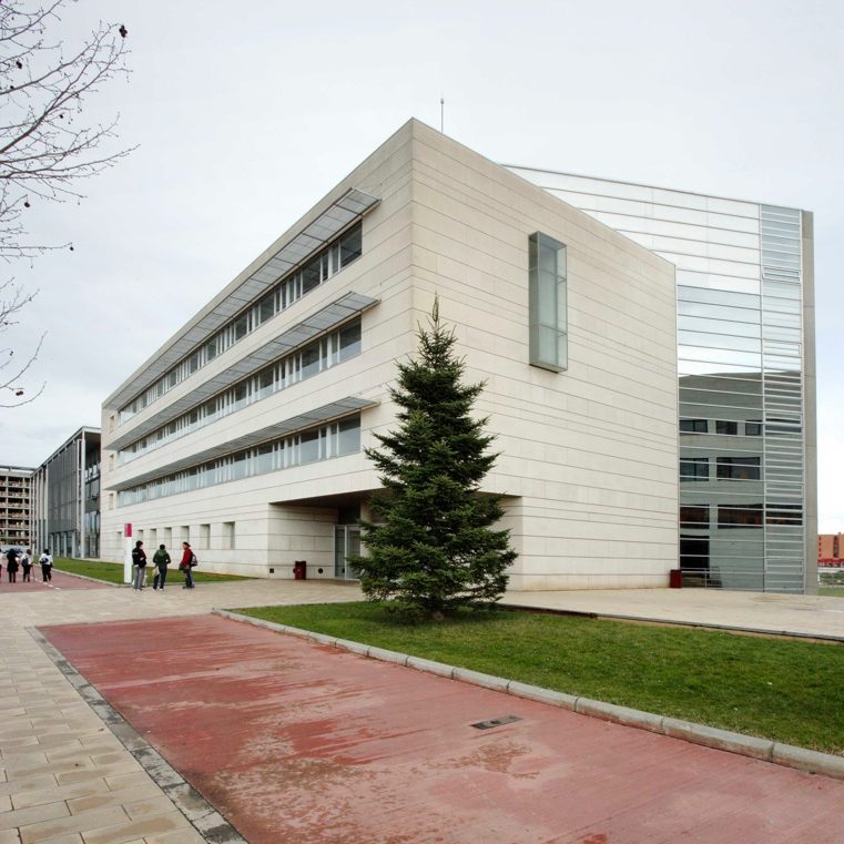 Façana principal d’un edifici modern de quatre plantes amb revestiment clar i finestres horitzontals. Es veuen arbres a l’esquerra i gespa al voltant de l’edifici. L'edifici és l'Escola Politècnica Superior de la Universitat de Lleida, al Campus de Cappont.